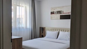 Ein modernes Schlafzimmer mit einem hölzernen Bett, weißer Bettwäsche, einem Kopfteil, einem Nachttisch und einer Deckenleuchte.