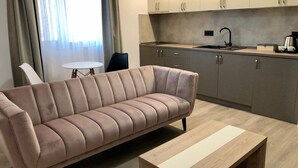 Ein modernes Wohnzimmer mit einer Couch und einem Couchtisch, einem kleinen runden Tisch und einer Küchenzeile mit Schränken und einer Spüle.