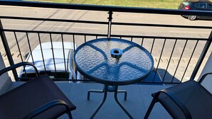 Een balkon met een ronde glazen tafel en twee stoelen.