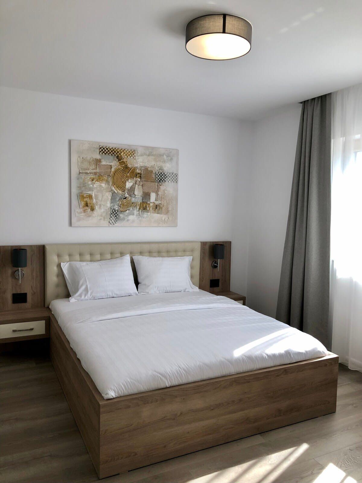 Ett modernt hotellrum med en säng i trä, en neutral färgskala och ett abstrakt konstverk på väggen.