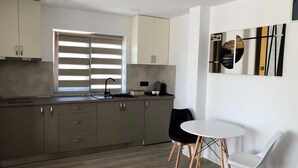 A modern kitchen with a large window, a dining area with two chairs, and a wall-mounted artwork.