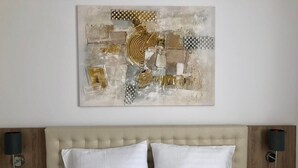 A hotel room with a tufted headboard, two white pillows, and a large abstract painting above the bed.