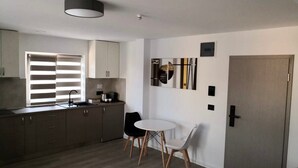 A modern kitchen with a dining area, featuring a white table and chairs, a built-in oven, and a window with blinds.