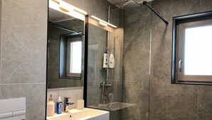 Ein modernes Badezimmer mit einer gläsernen Dusche, einem weißen Waschbecken und einem großen Spiegel.