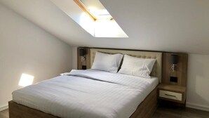 Ein Schlafzimmer mit Dachfenster, einem Bett mit weißer Bettwäsche, einem Holz-Kopfteil, Nachttischen mit Lampen und einem Holzboden.