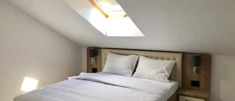 A bedroom with a skylight, a bed with white bedding, wooden headboard, bedside tables with lamps, and a wooden floor.