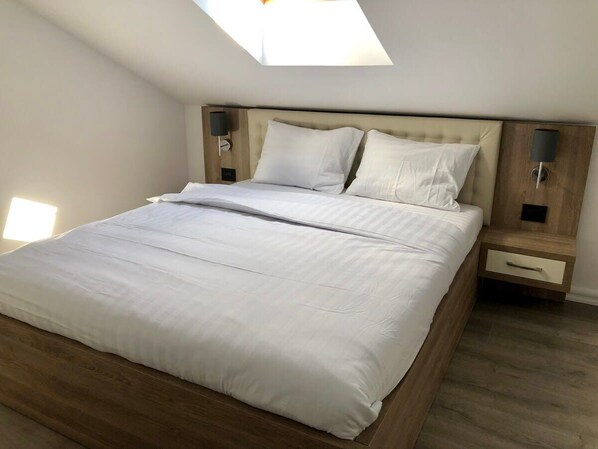 A modern bedroom with a wooden bed, white linens, a skylight, and bedside lamps.