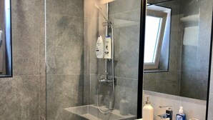 Uma casa de banho moderna com cabine de duche em vidro, lavatório branco com espelho e artigos de higiene pessoal.