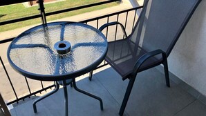 Mesa com tampo de vidro, estrutura metálica e cadeira de tela em uma varanda.