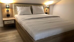 Quarto moderno com estrutura de cama de madeira, roupa de cama branca e duas luminárias de cabeceira.