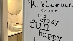 Un bagno con uno specchio tondo, un lavandino bianco e una parete con una citazione motivazionale.