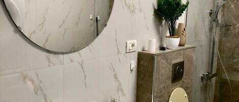 Un baño moderno con un espejo redondo, un lavabo blanco, un inodoro y una ducha.