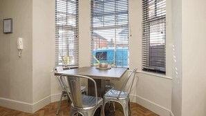 A dining area with a wooden table, two metal chairs, and a window with blinds.