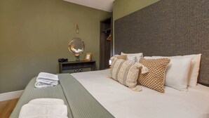 A neatly made bed with white and patterned pillows, a bedside table with a mirror, and a green wall.