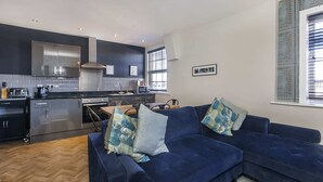 A modern kitchen with stainless steel appliances, a dark blue sofa with patterned cushions, and a dining area with a table and chairs. - 3 bedroom apartment in central York (York)
