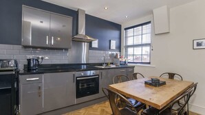 A modern kitchen with stainless steel appliances, a wooden dining table, and a window with blinds. - 3 bedroom apartment in central York (York)