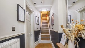 A narrow hallway with a carpeted floor, a staircase, and a white vase with dried flowers on a wooden table. - 3 bedroom apartment in central York (York)