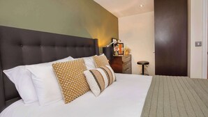 A neatly made bed with a dark headboard, a bedside table with a lamp, and a small stool. - Luxury Two Bedroom Apartment Apt 4 (York)