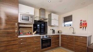 A modern kitchen with wooden cabinets, a built-in oven, a microwave, and a stainless steel range hood. - Luxury Two Bedroom Apartment Apt 4 (York)