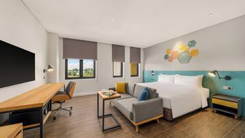A modern hotel room with a wooden desk, a sofa, a bed, and a nightstand.
