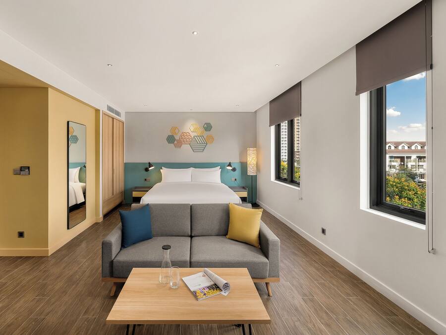 A modern hotel room with a large bed, a sofa, a coffee table, and a view of the city.