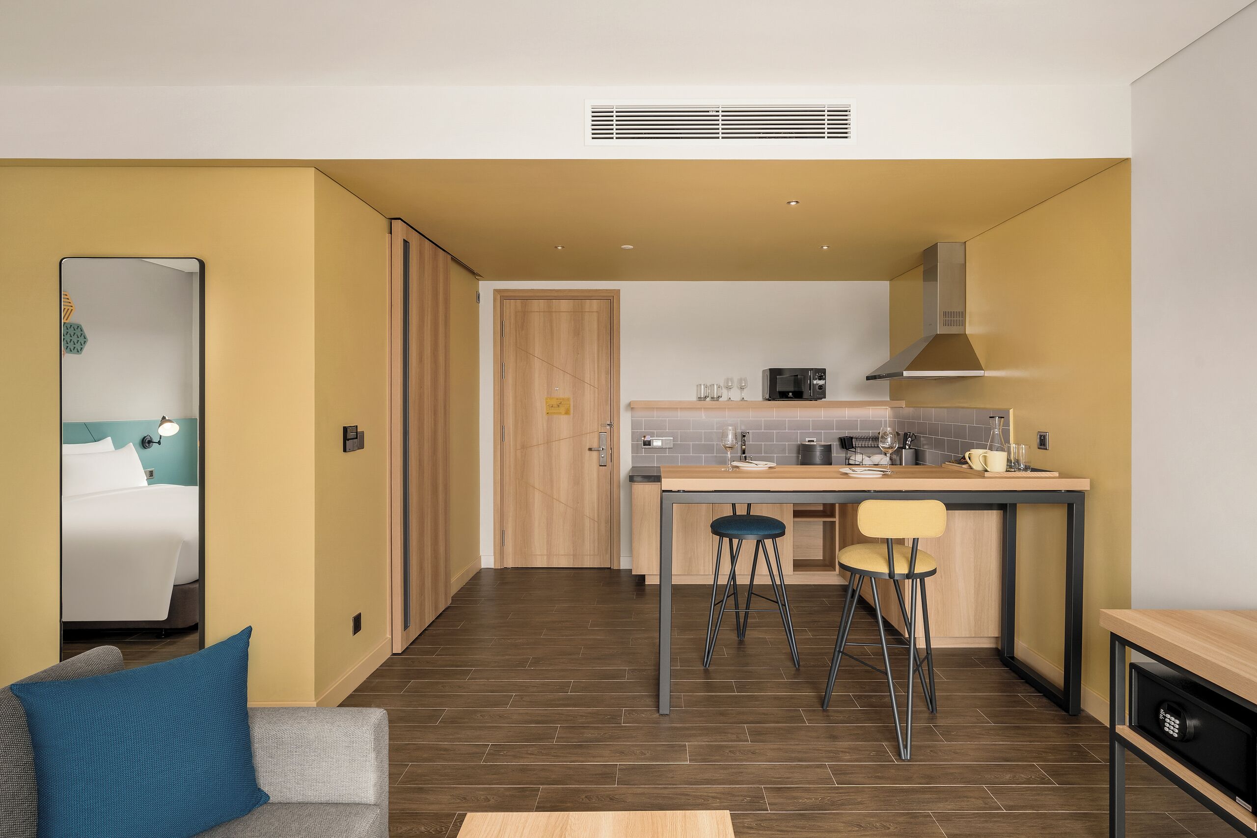 A compact hotel room with a bed, a small sitting area, and a kitchenette.