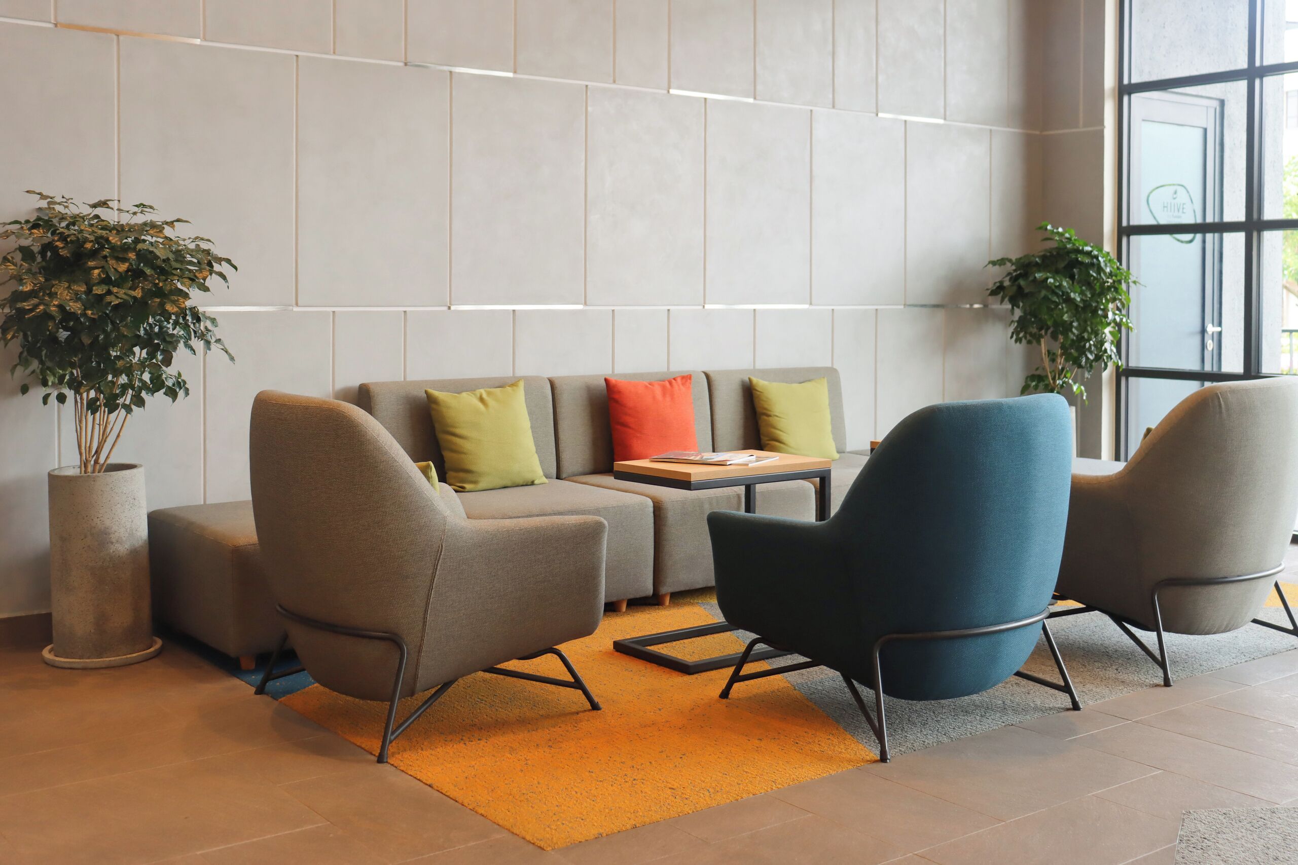 Un espacio lounge moderno con un sofá, dos sillones, una mesita y dos plantas en macetas.
