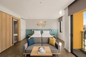 Ein modernes Hotelzimmer mit einer Sitzecke, zwei Betten, einem Couchtisch und Blick nach außen.