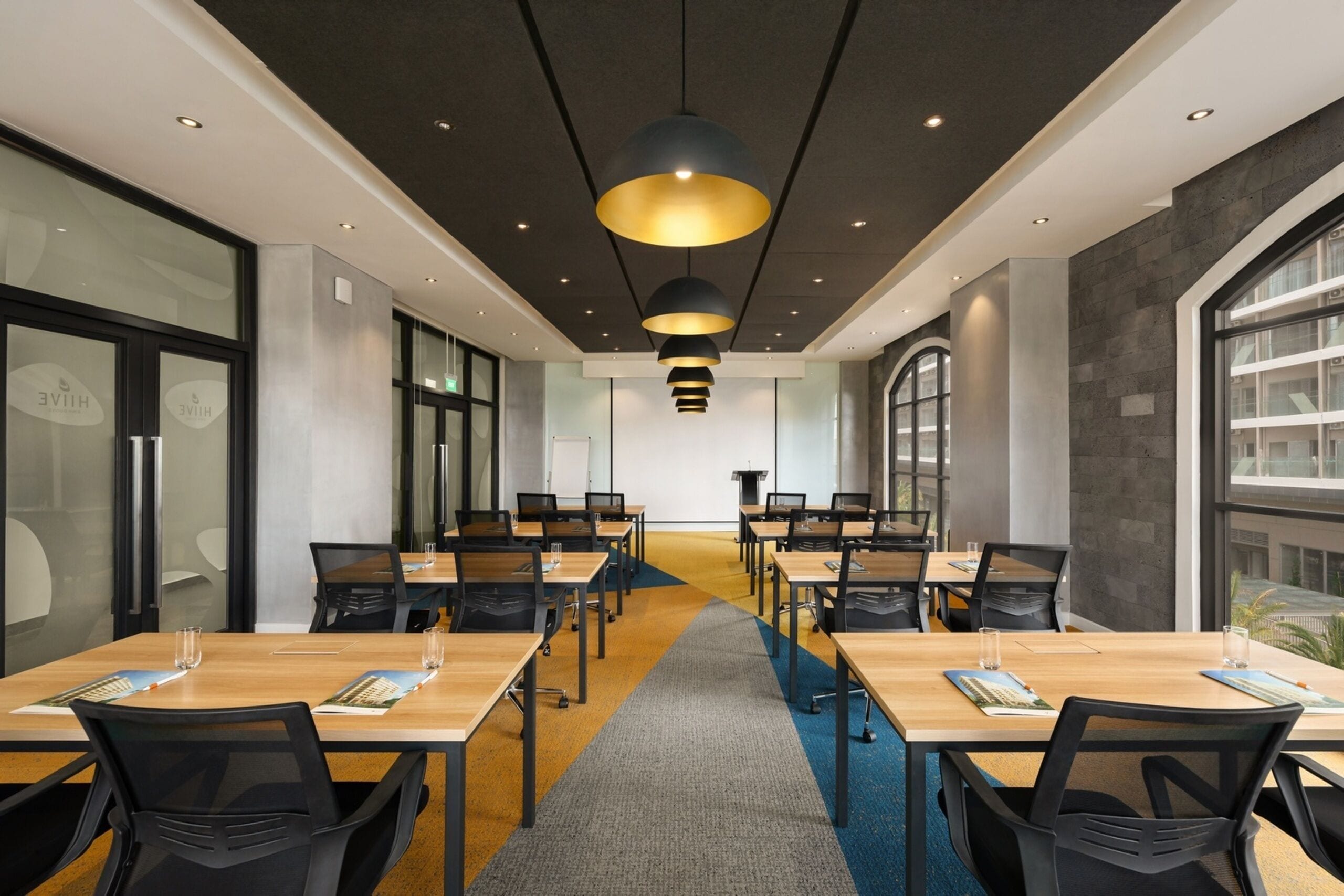 A conference room with multiple tables and chairs, a central aisle, and pendant lighting.