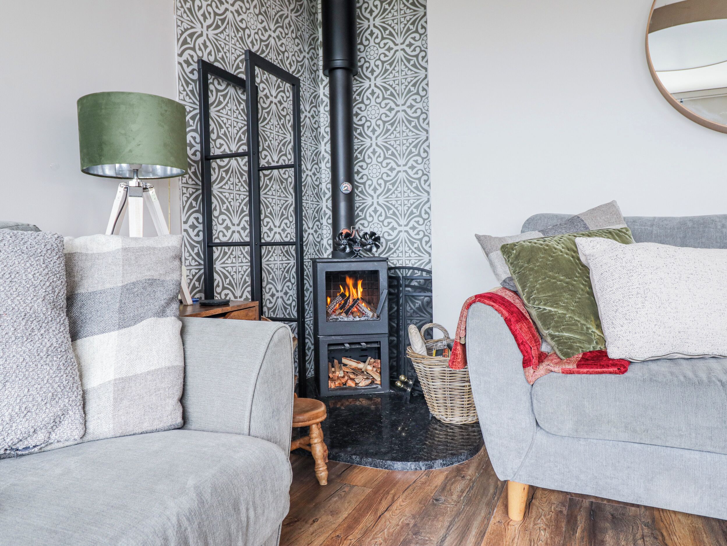 A cozy living room with a fireplace, patterned wallpaper, and a round mirror.