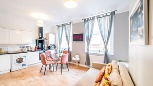 A modern kitchen with white cabinets, a black range hood, and a dining area with pink chairs. - [Covent Garden]Central London Apartment (London)