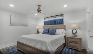 A bedroom with a bed, two bedside tables, a ceiling fan, a painting, and a door.