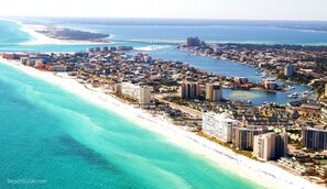 An aerial view of a coastal city with a long beachfront, dense urban area, and a marina with boats.