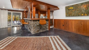 Una cocina moderna con una isla de piedra, techo de madera y sillas anaranjadas.
