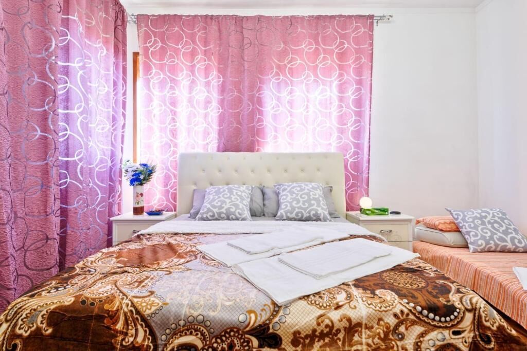 A bedroom with a patterned bedspread, a tufted headboard, and a nightstand with a vase of flowers.