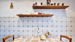 A dining area with a round table, chairs, a patterned tablecloth, and a decorative shelf above. - Apt Venice City (Mestre)