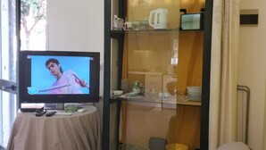 A living room with a television, a table with remote controls, and a glass-fronted cabinet with kitchen items. - Apartment a few minutes from the Sea (Letojanni)