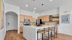 A modern kitchen with a central island, wooden flooring, and pendant lighting. - Desert Rose - Tiki Game-room, 10 min to Indian wells tennis garden Festivals, Golf and more! (Indio)