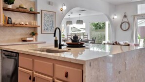 A modern kitchen with a large island, built-in appliances, and a view to the dining area. - Desert Rose - Tiki Game-room, 10 min to Indian wells tennis garden Festivals, Golf and more! (Indio)