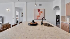 A modern kitchen with a large island, a black faucet, and a marble countertop. - Desert Rose - Tiki Game-room, 10 min to Indian wells tennis garden Festivals, Golf and more! (Indio)