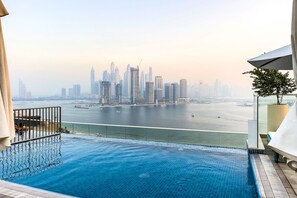 An infinity pool with a city skyline view, a balcony with a railing, and a potted plant. - New modern studio on Palm Jumeirah (Dubai)