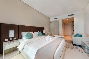 A modern hotel room with a large bed, a bedside table with a lamp, a small round table, and a seating area with a sofa and armchair. - New modern studio on Palm Jumeirah (Dubai)