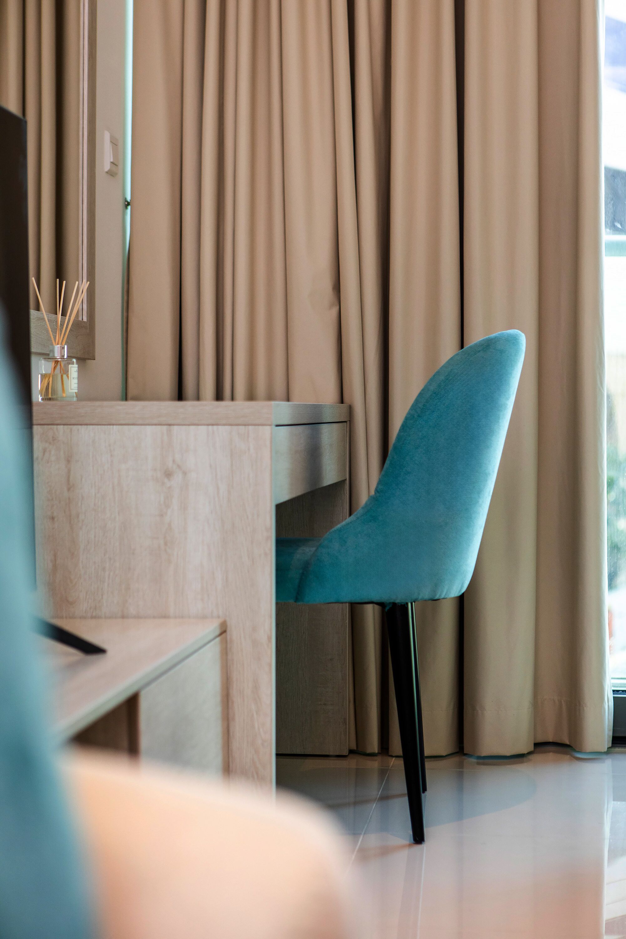 A modern room with a wooden desk, a blue chair, and beige curtains.
