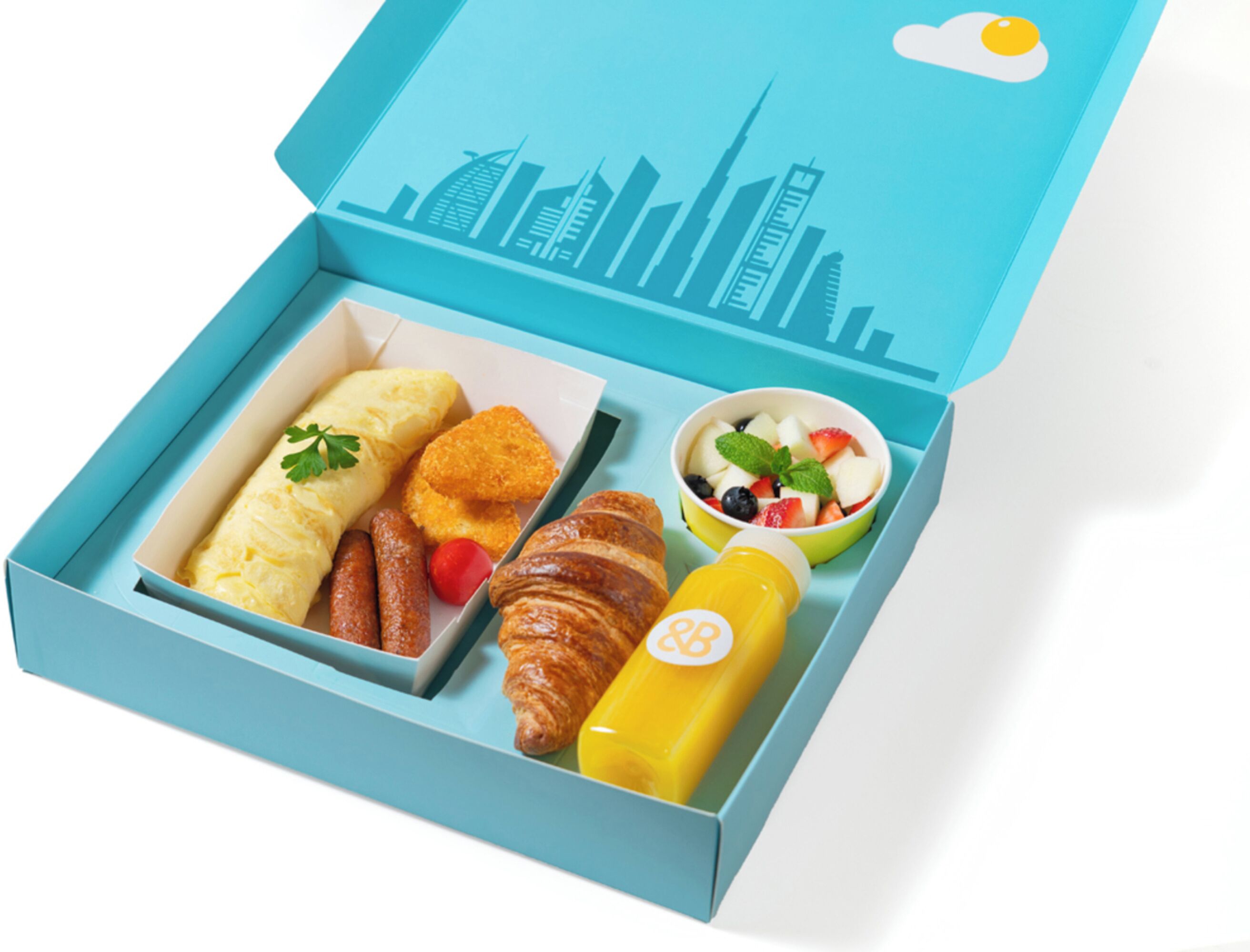 A breakfast box with croissants, sausages, scrambled eggs, and a fruit bowl.
