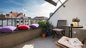 Un balcon donnant sur des immeubles, une table avec une chaise et une plante en pot.
