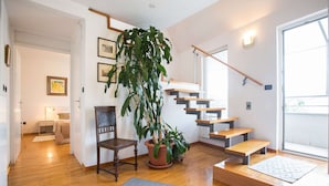 Un salon moderne avec un escalier, un plancher en bois, une grande plante en pot et un lit avec une table de chevet.