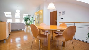 Une pièce moderne et bien éclairée, avec une table ronde en bois et quatre chaises, un canapé gris et une grande plante en pot.