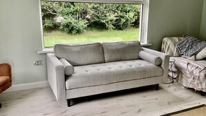 A grey sofa in a room with a window overlooking a garden.