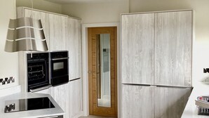 A modern kitchen with white cabinetry, a built-in oven, a stainless steel range hood, and a wooden door.
