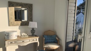 Une chambre à coucher comprenant un lit, une commode, une chaise, une lampe, un miroir et une porte-fenêtre coulissante donnant sur un espace extérieur.